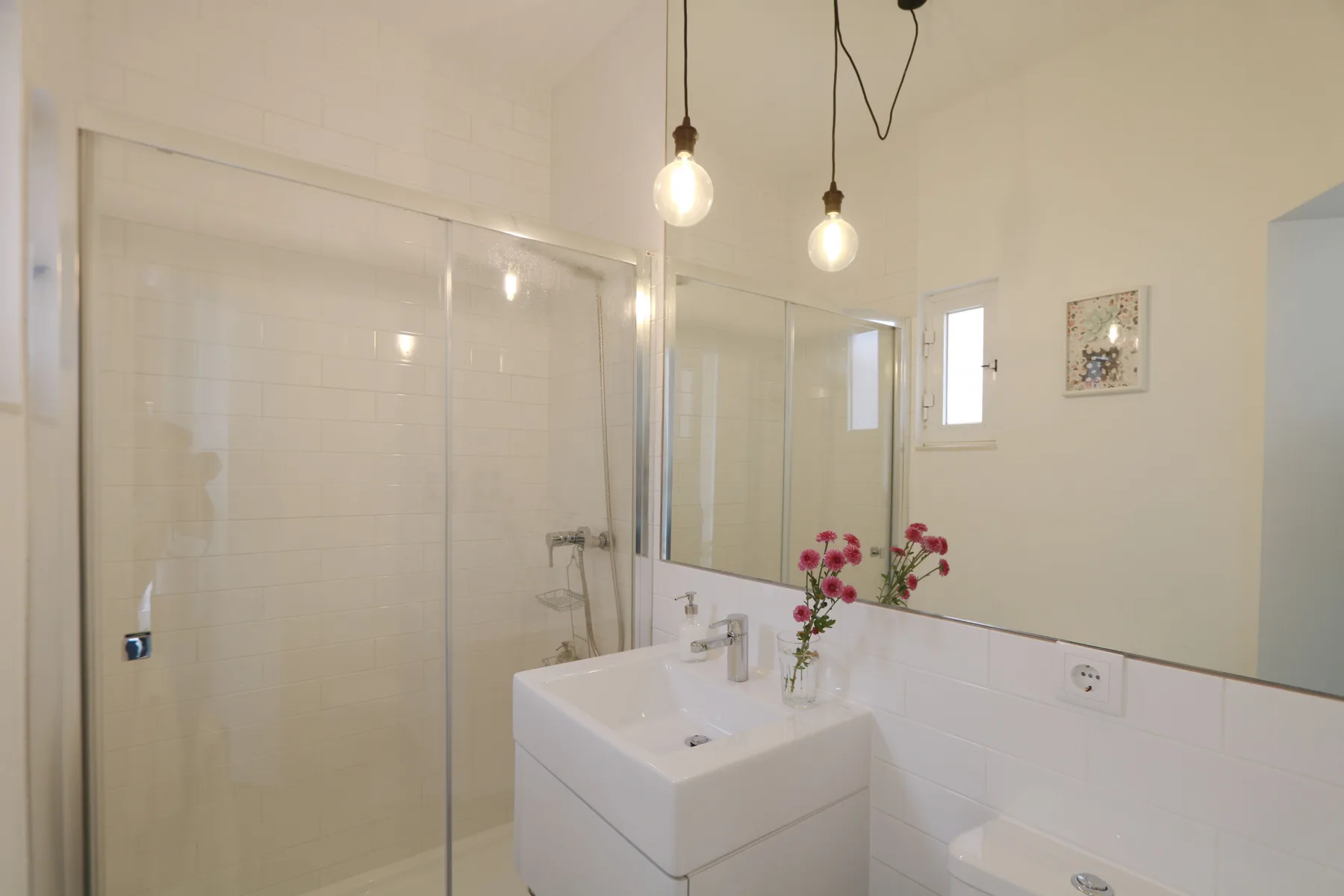 Un baño luminoso con una ducha de cristal y un lavabo blanco.