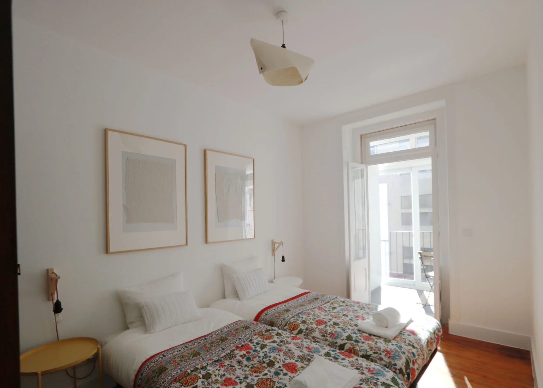 Un dormitorio luminoso con camas y una puerta abierta a un balcón.