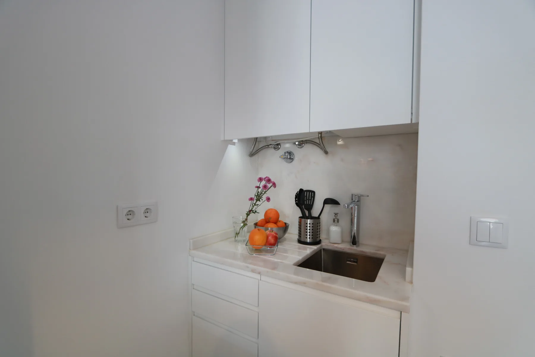 Una cocina compacta con armarios blancos, una encimera y un fregadero.