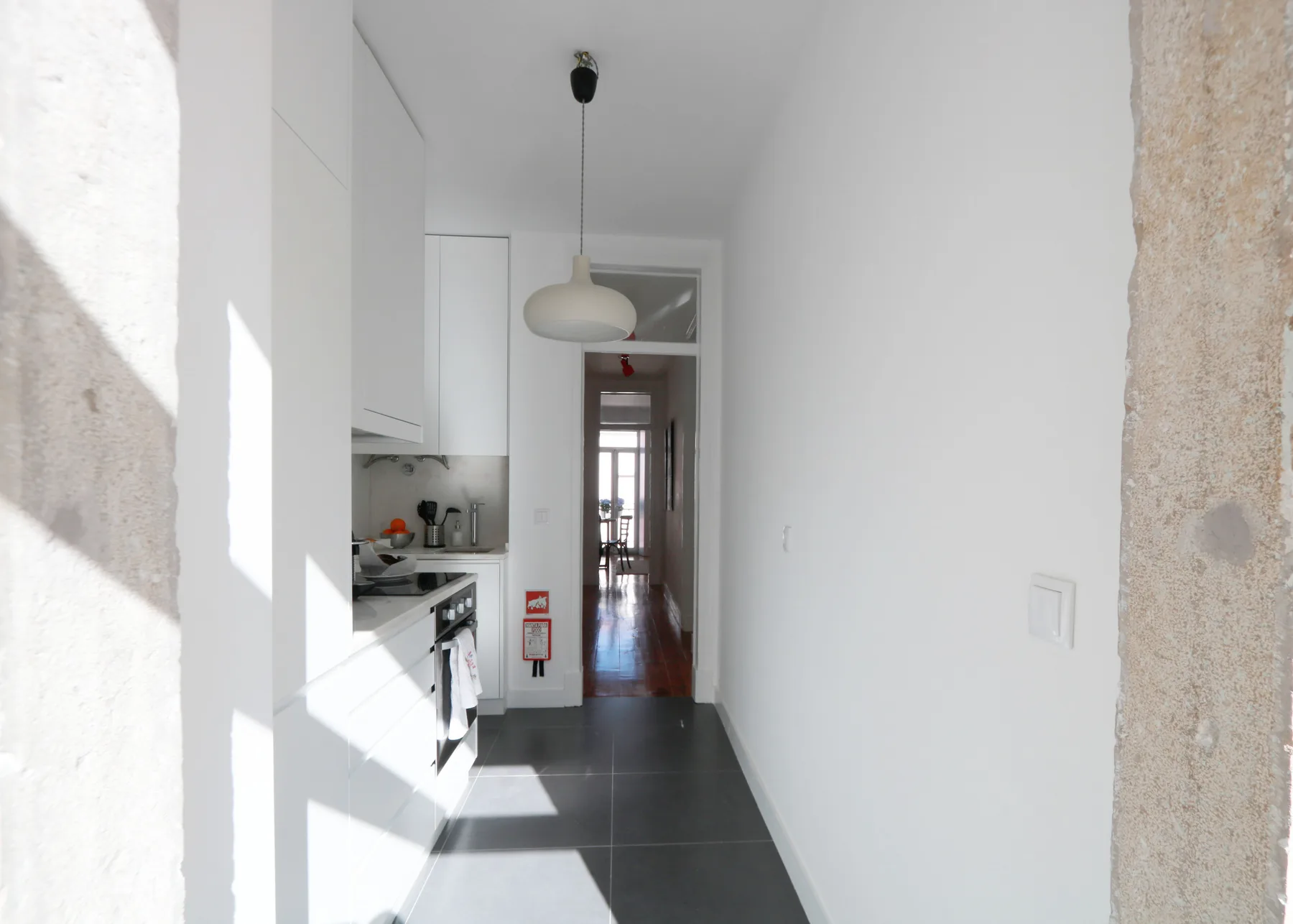 Una cocina luminosa da a un pasillo estrecho con suelo de baldosas oscuras.
