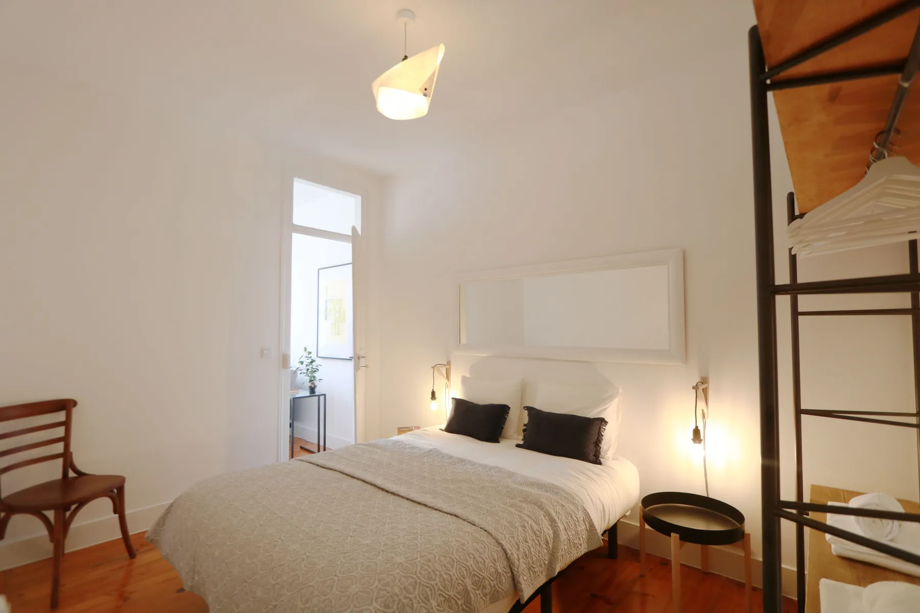 Dormitorio con una cama bien hecha, luces junto a la cama y suelo de madera.