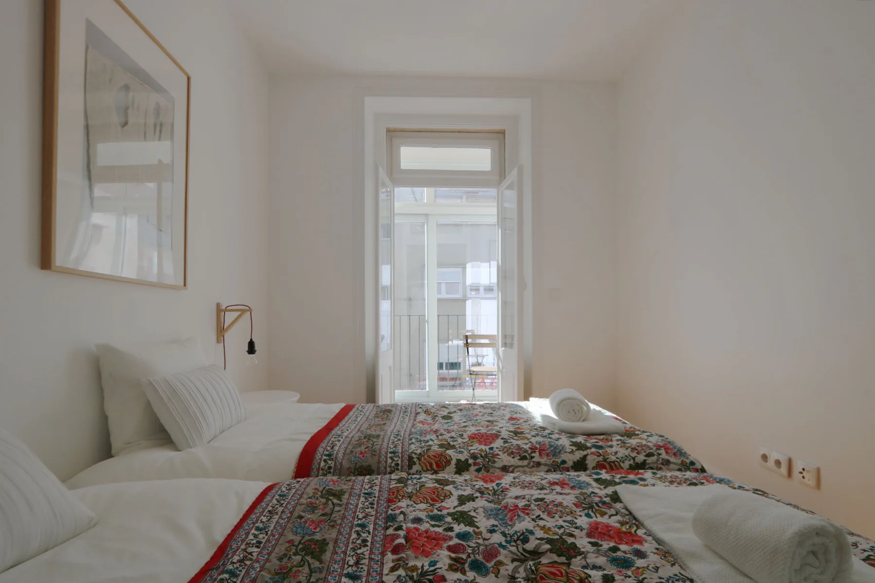 Un dormitorio con dos camas cubiertas con colchas estampadas junto a una ventana alta.