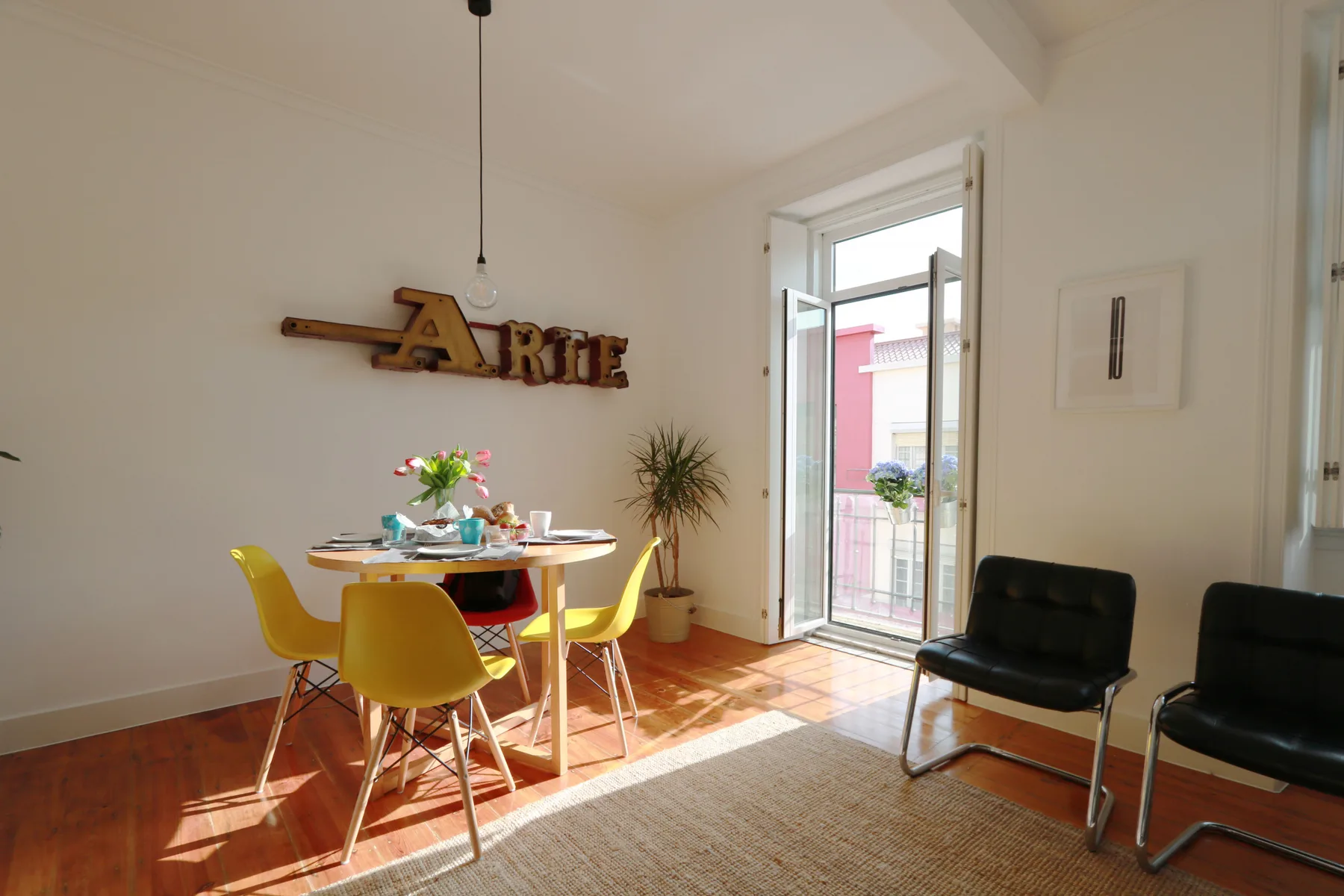 Un comedor luminoso con una mesa, asientos amarillos y una puerta abierta al balcón.