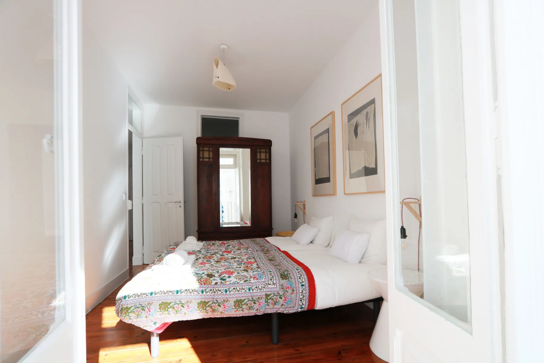 Un dormitorio luminoso con una colcha estampada y cuadros enmarcados.