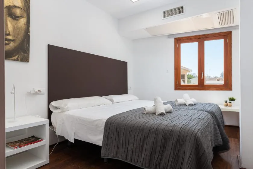 A bright bedroom with a bed dressed in white linens and a dark gray cover.