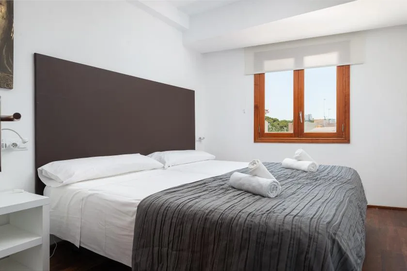 A bedroom with a neatly made bed and a window overlooking greenery.