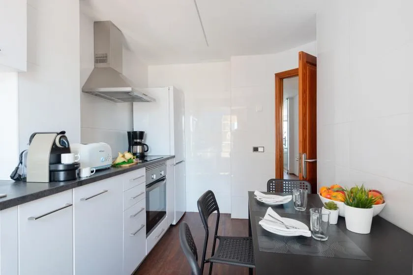 A bright kitchen with white cabinetry and a dining table set with dishes.