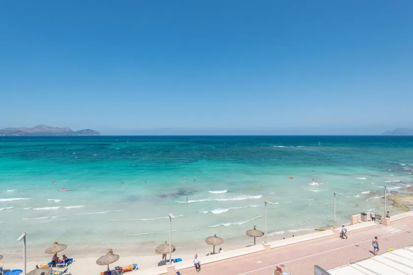 A beach promenade borders turquoise water beneath a clear blue sky.