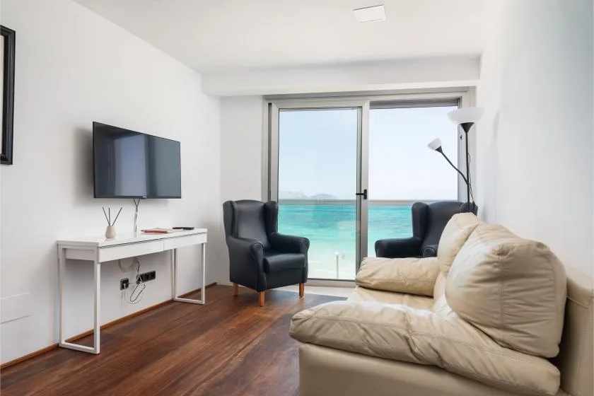 A bright living room with seating, a television, and glass doors overlooking the sea.