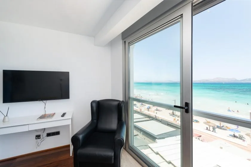 A room with a television and armchair beside glass doors overlooking a beach and sea.