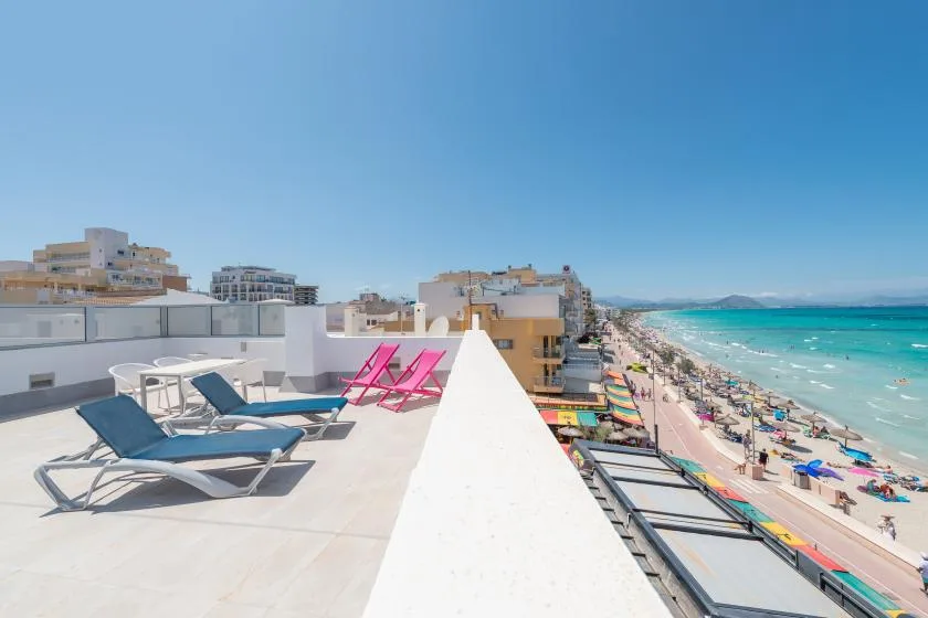 A sunny rooftop terrace overlooks a long beach and turquoise water.