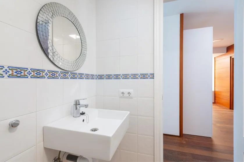 A tiled bathroom with a white sink and round wall mirror.