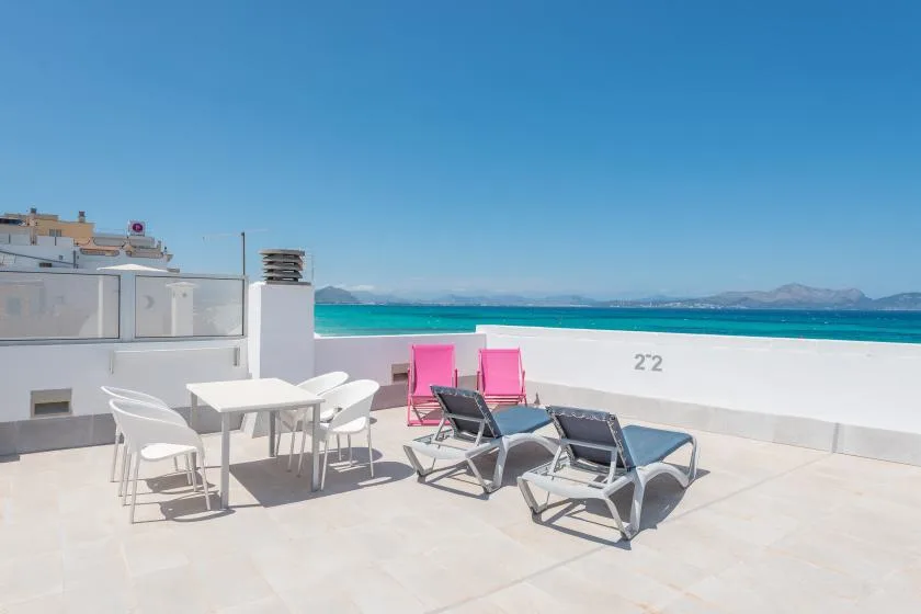 A sunny rooftop terrace overlooks the sea, with lounge chairs and a dining table.