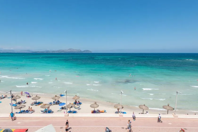 A beach with turquoise water, small waves, and people swimming near the shore.