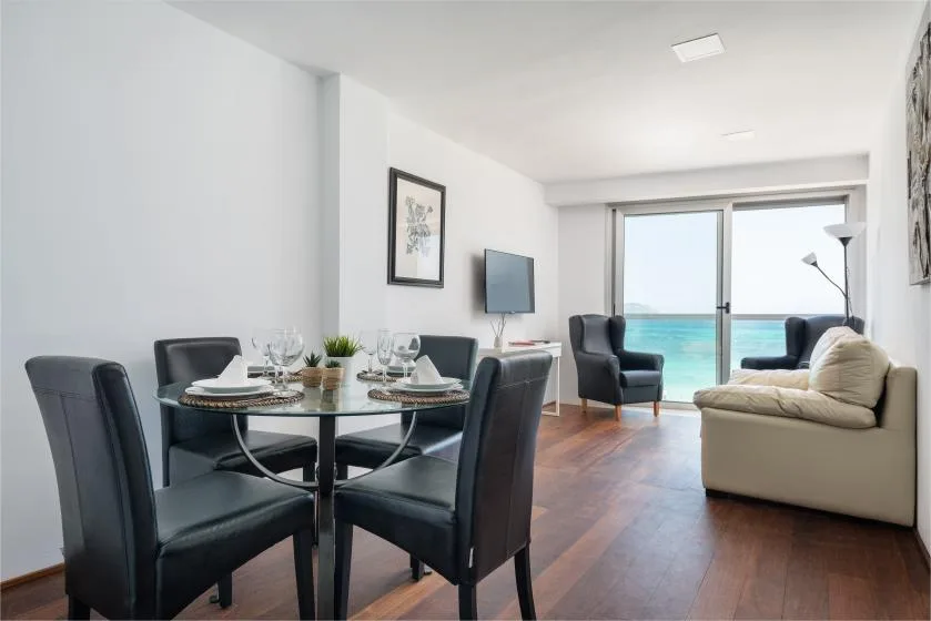 A bright living and dining area with seating beside large windows overlooking the water.