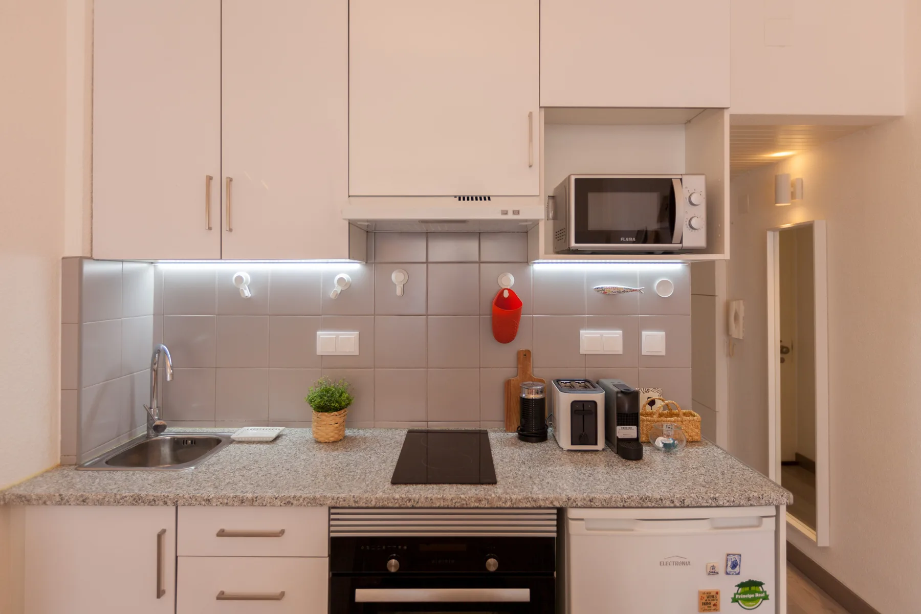 A compact kitchen with white cabinets, tiled backsplash, and a countertop.