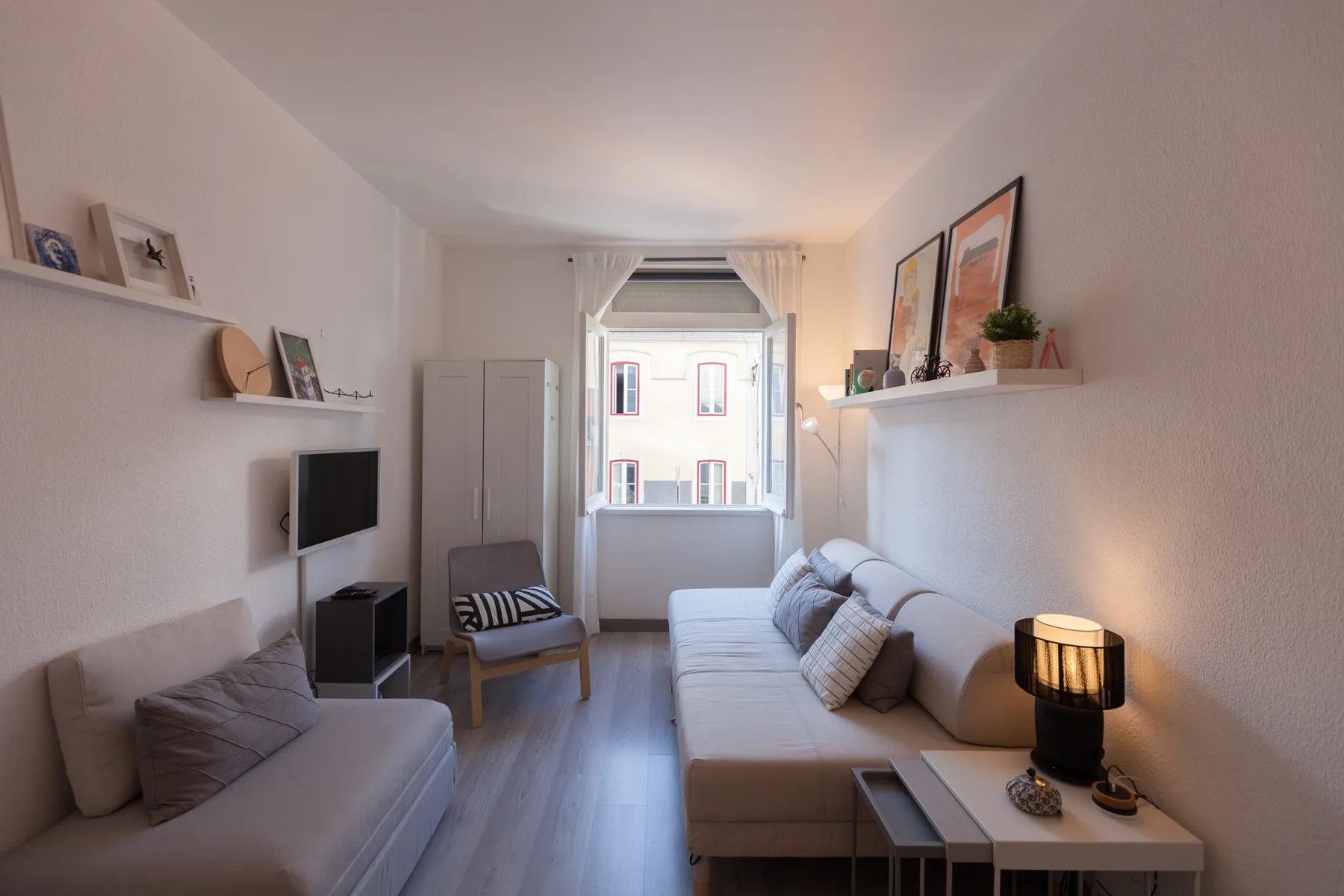 A bright living room with seating, a television, and a window at the far end.