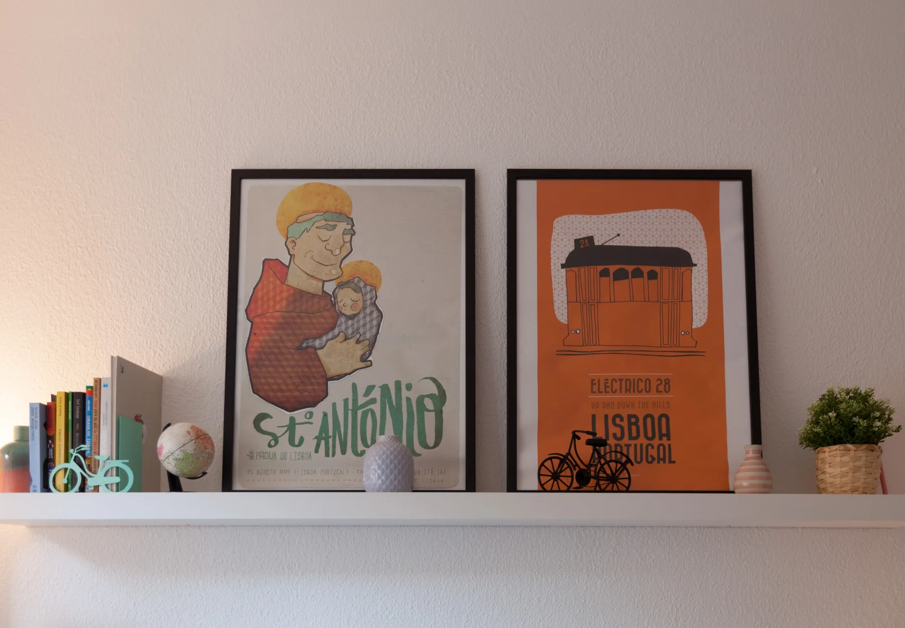 Two framed posters hang above a shelf against a white wall.