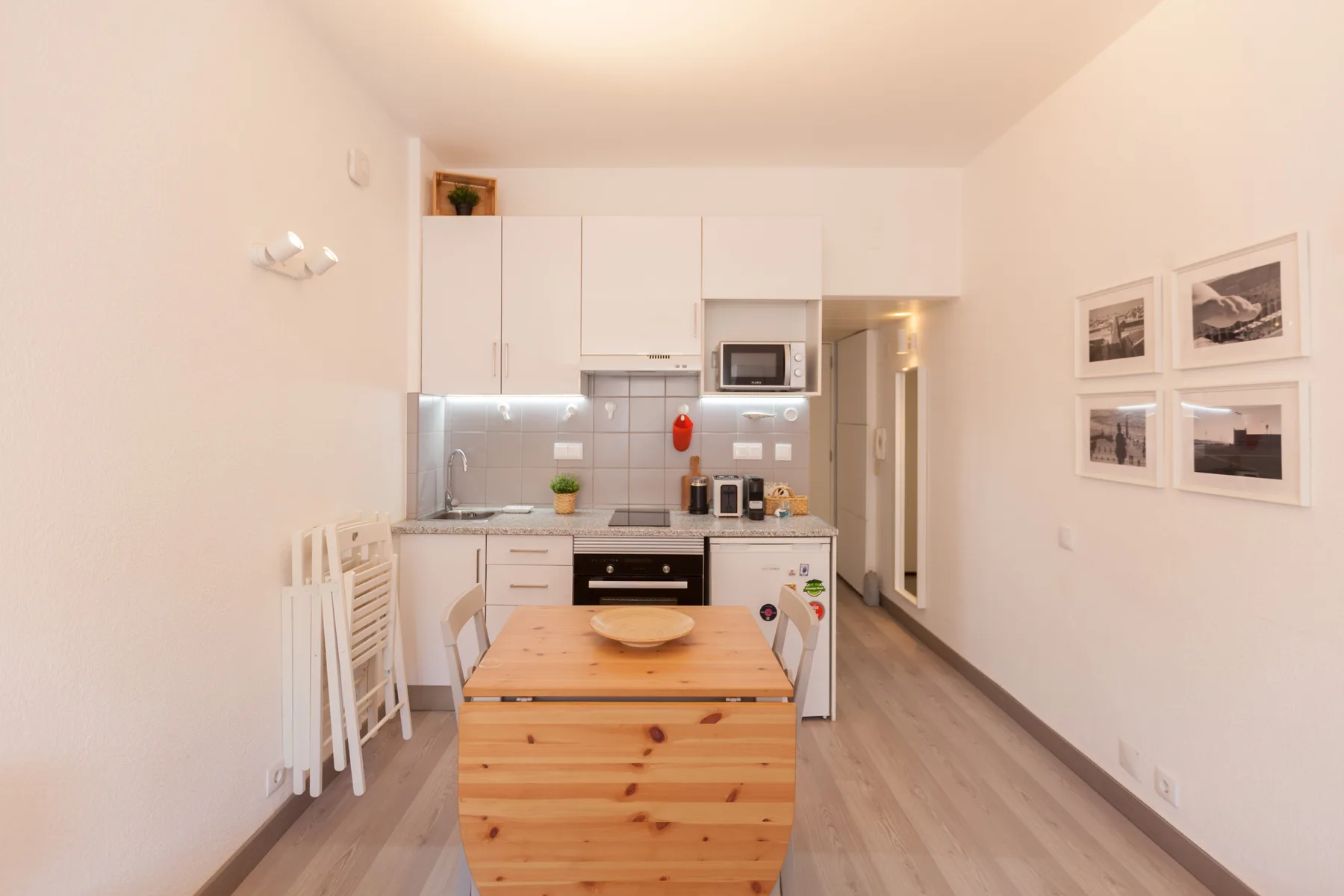 A compact kitchen and dining area with a wooden table and framed pictures on the wall.
