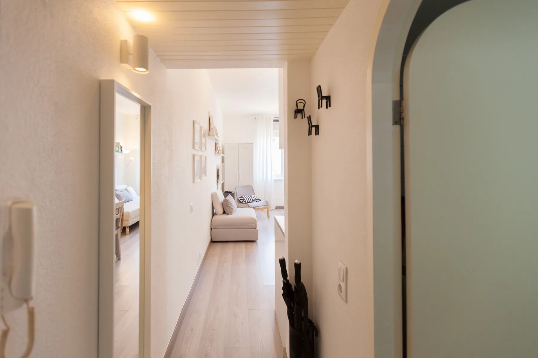 A bright hallway opens toward a living area with seating and a window.