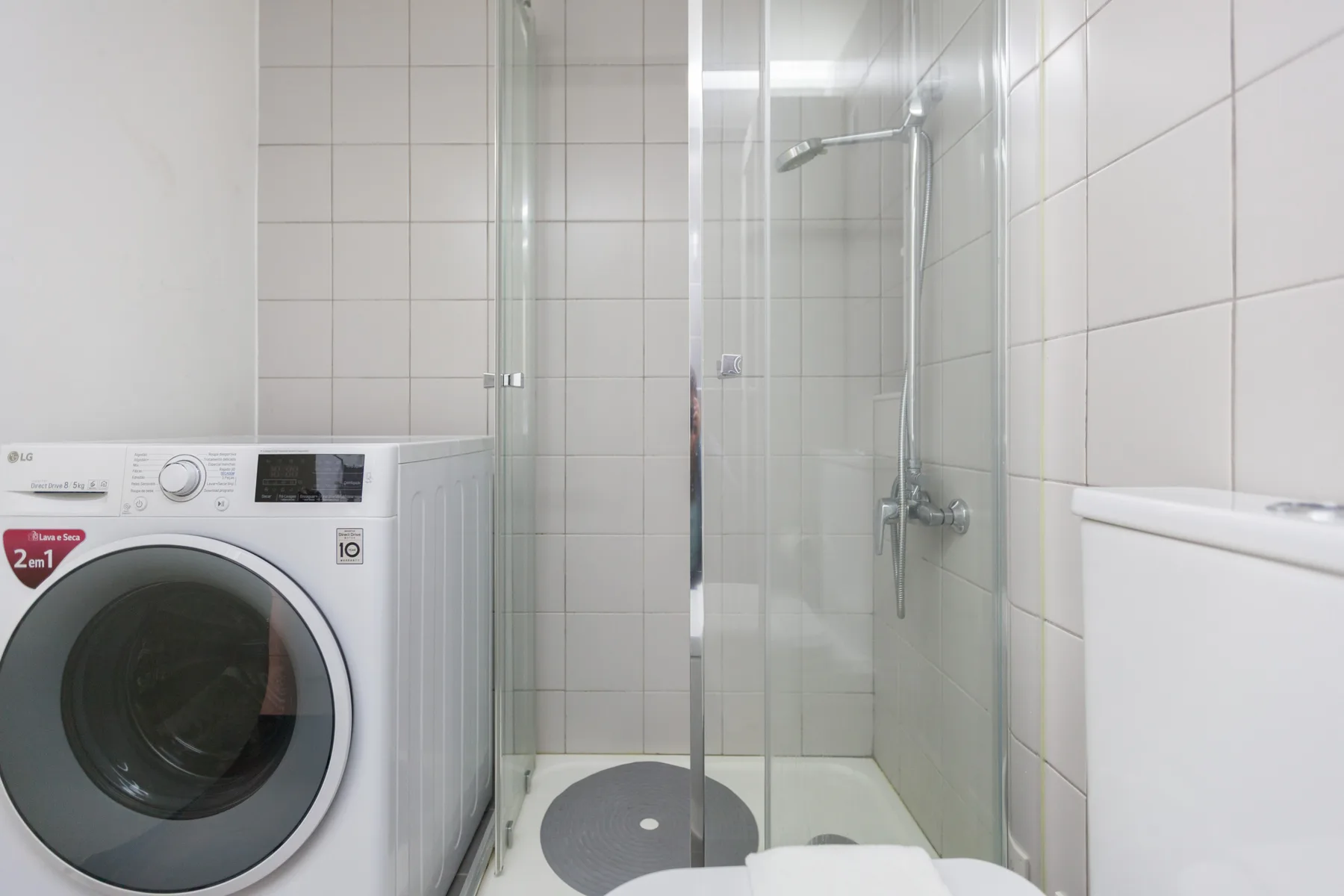 A tiled bathroom with a shower and washing machine.