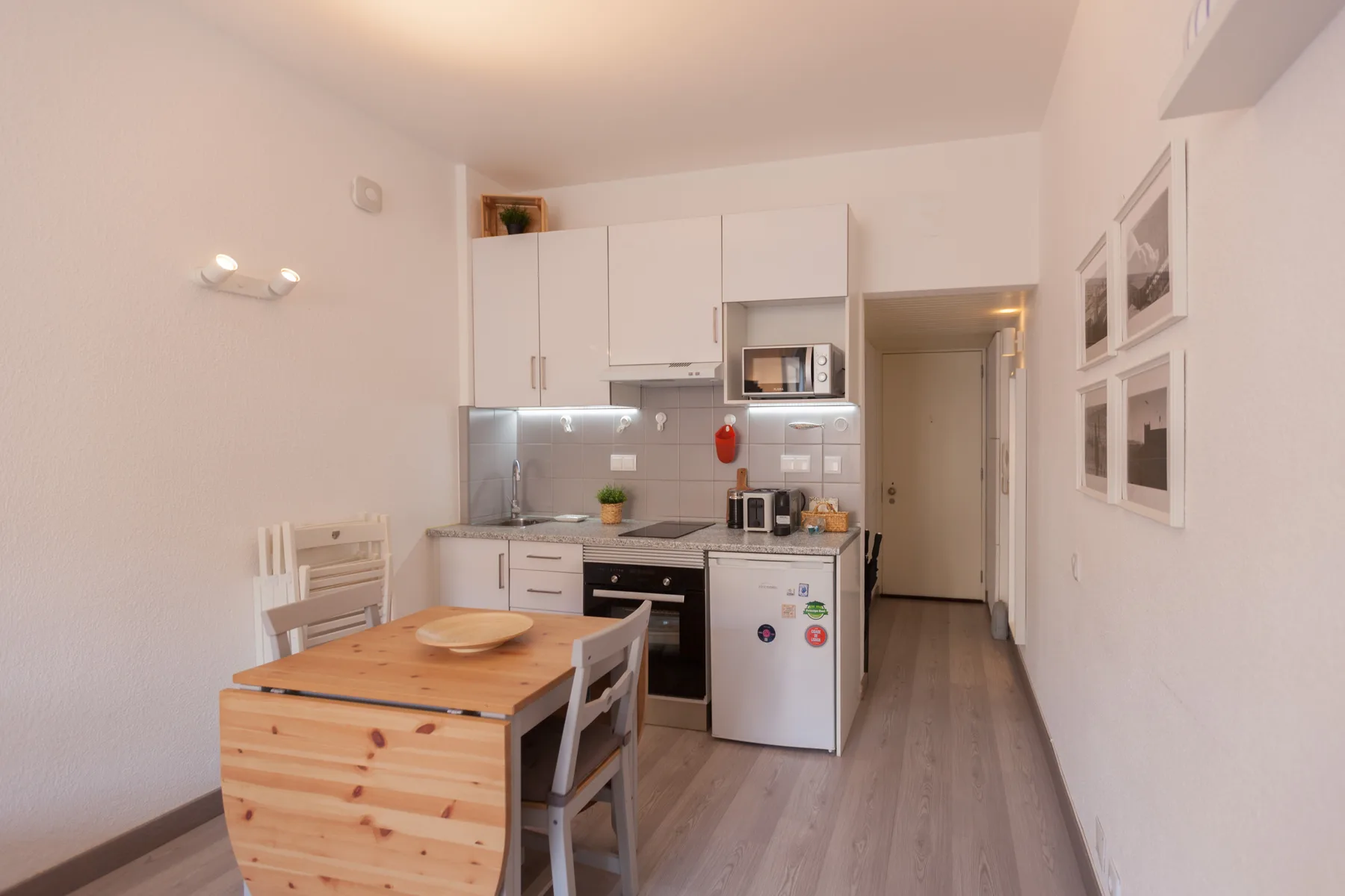 A compact studio kitchen and dining area with a wooden table.