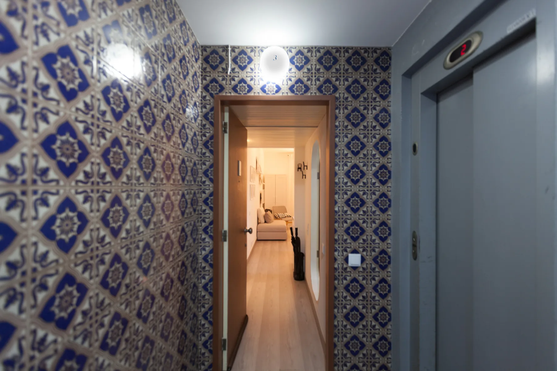 A tiled hallway opens onto a warmly lit room beside an elevator.