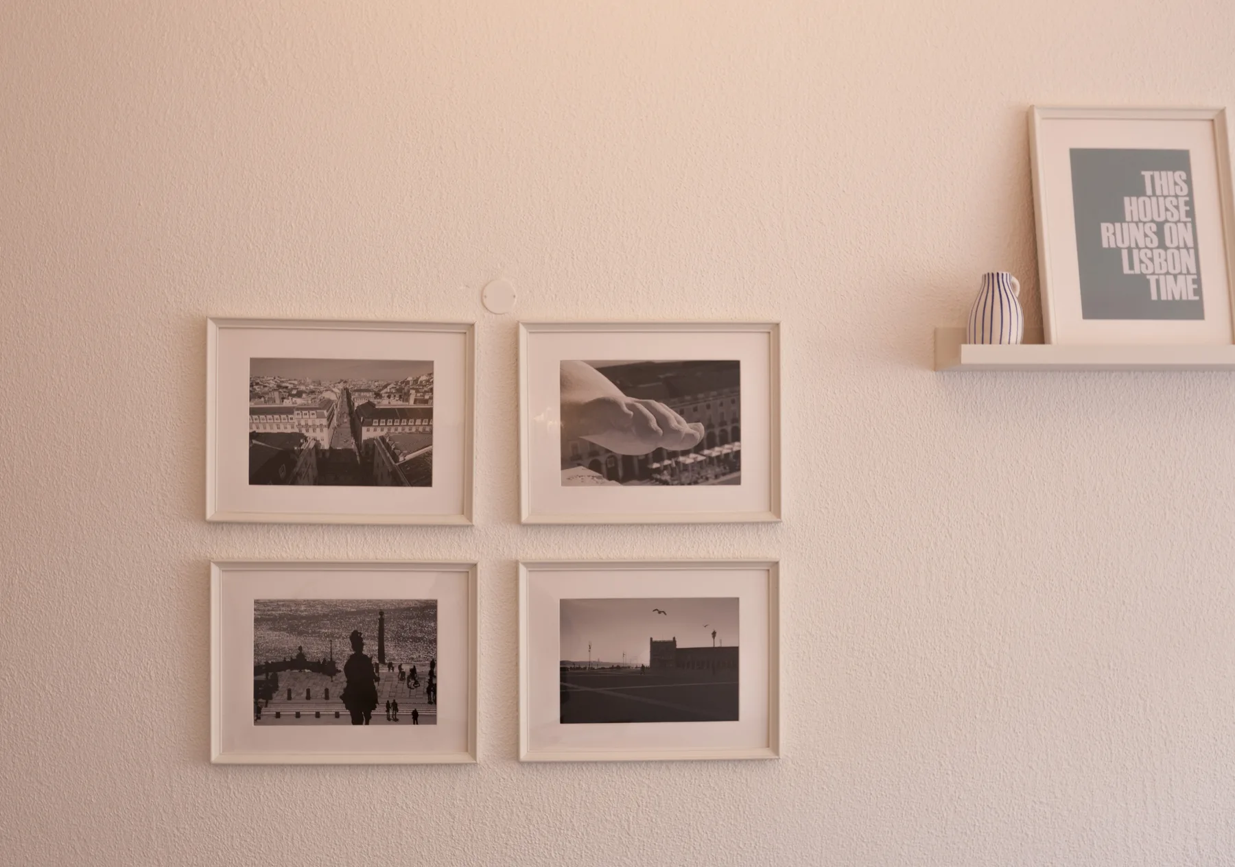 A light-colored wall displays four framed photographs and a small shelf with a framed print.