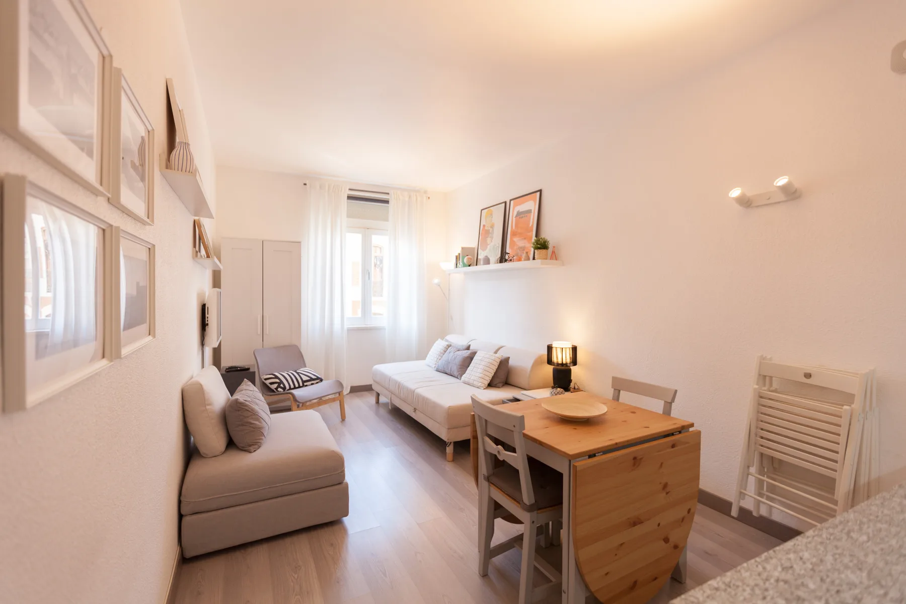 A bright studio living area with seating, a bed, and a dining table.