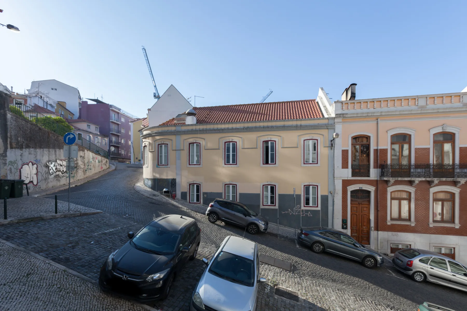 A cobblestone street runs between colorful buildings with parked cars.