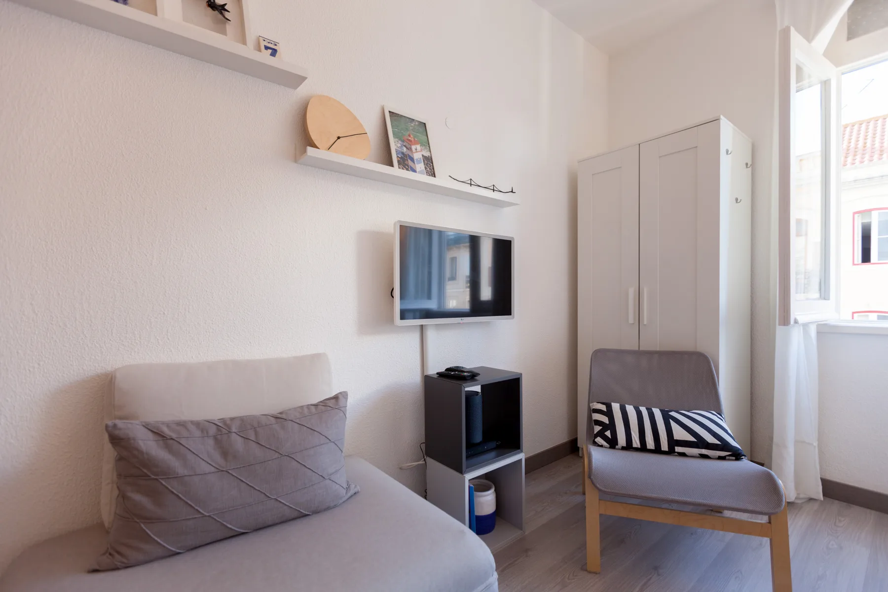 A bright living area with seating, a wall-mounted television, and a tall cabinet.