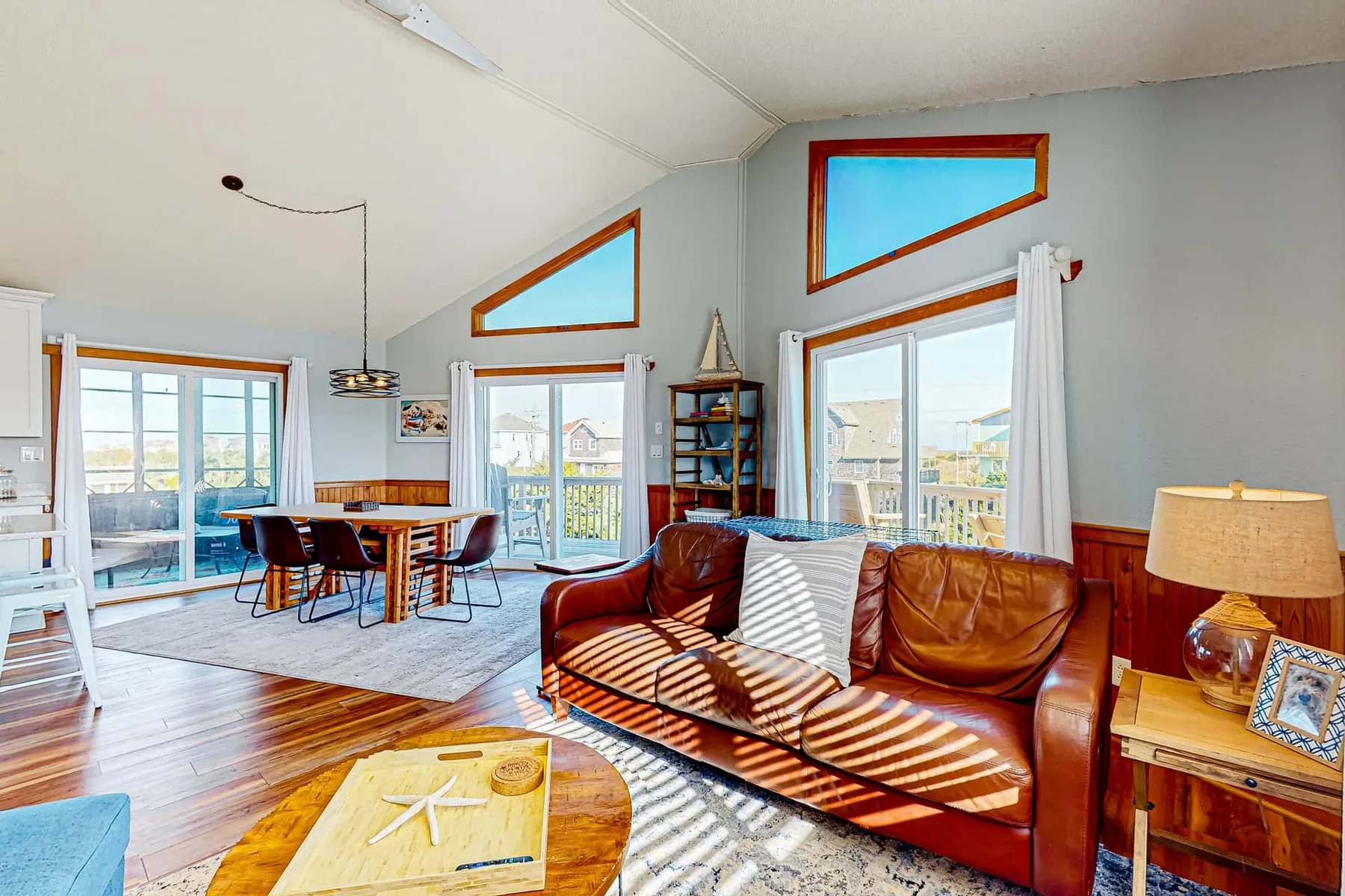 A bright living and dining area with leather seating, a dining table, and large windows.