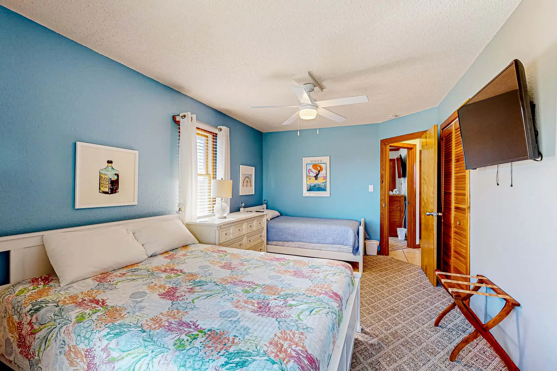 A blue bedroom with a floral bedspread, a small sofa, and a wall-mounted television.