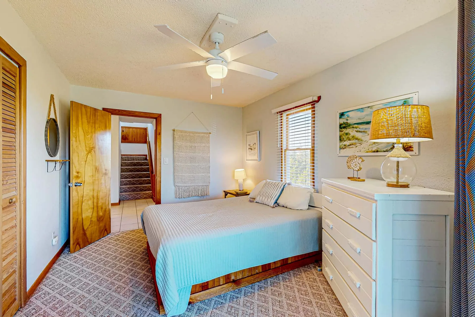 A bedroom with a bed, a ceiling fan, and a dresser.