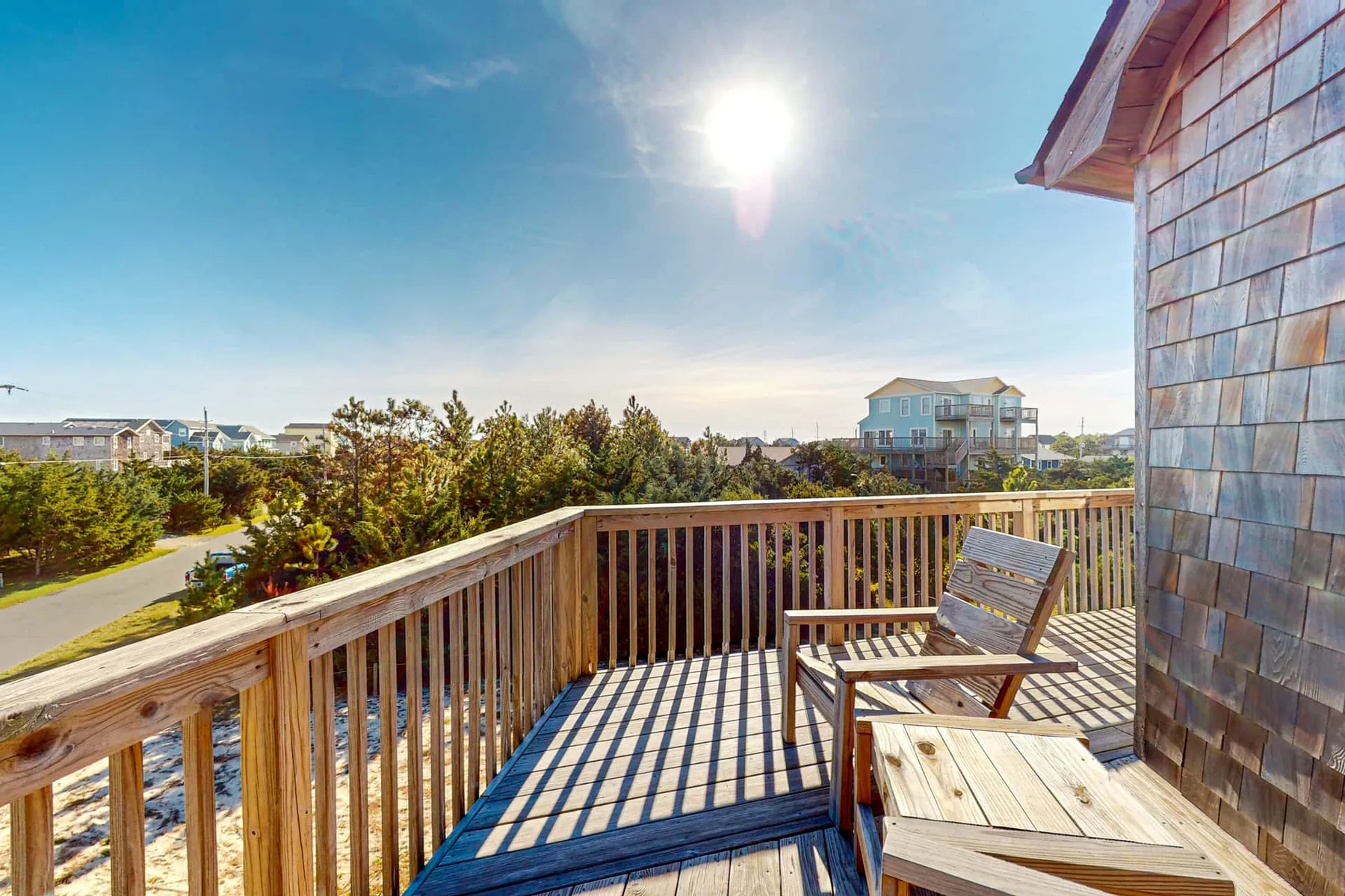 A wooden deck with seating overlooks trees and nearby buildings under a bright sky.