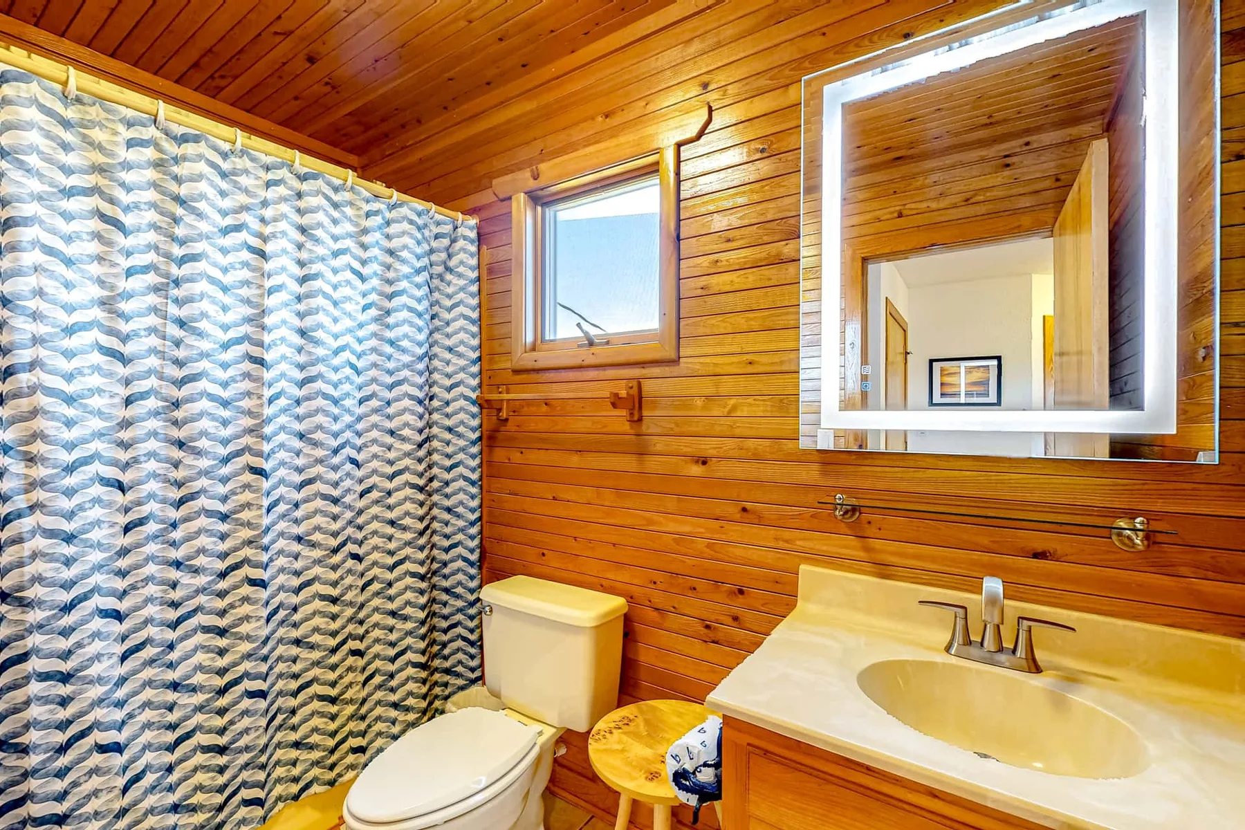 A wood-paneled bathroom has a bathtub-shower area, sink, and wall mirror.