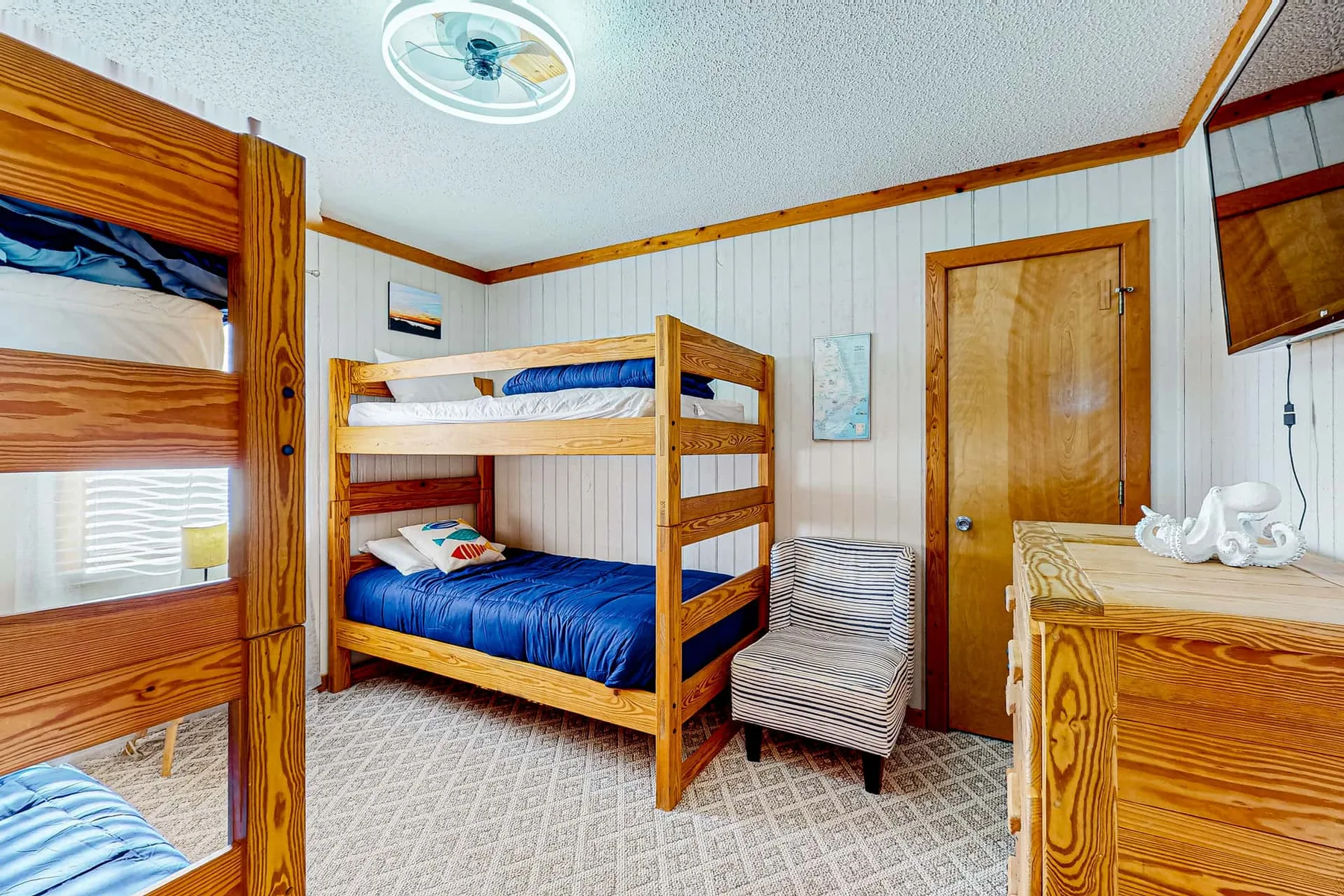A bedroom with wooden bunk beds, blue bedding, and a small upholstered seat.