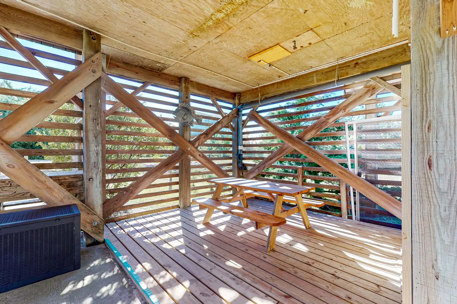 A covered wooden deck with a picnic table and slatted walls.