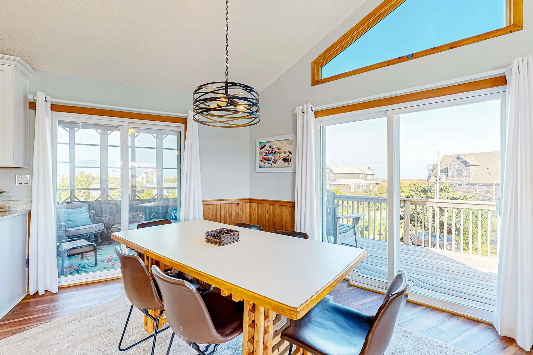 A bright dining area with a long table beside large windows and a balcony.