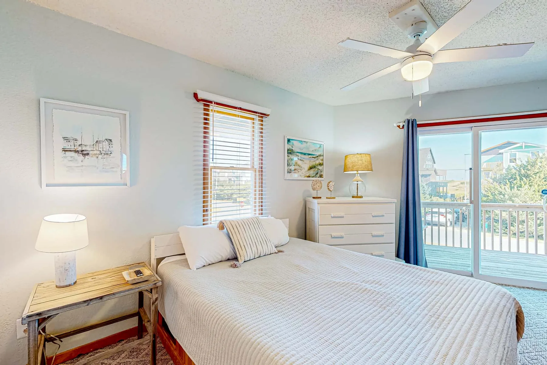 A bright bedroom with a neatly made bed beside a sliding glass door.