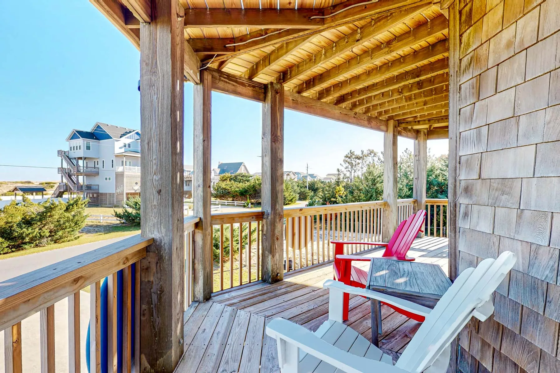 A covered wooden porch with outdoor seating and a railing overlooking the surrounding area.
