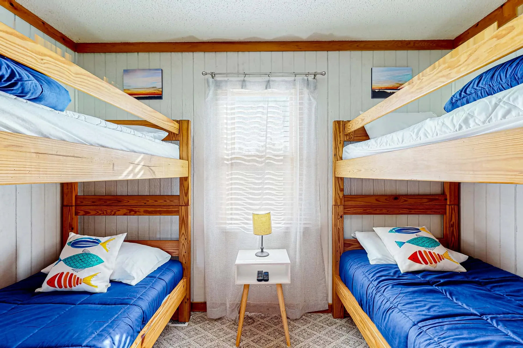 A bedroom with wooden bunk beds, blue bedding, and a small table by the window.