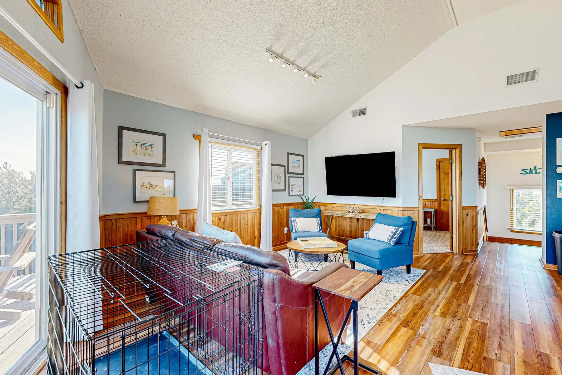A bright living room with seating, a television, and a large metal pet crate.