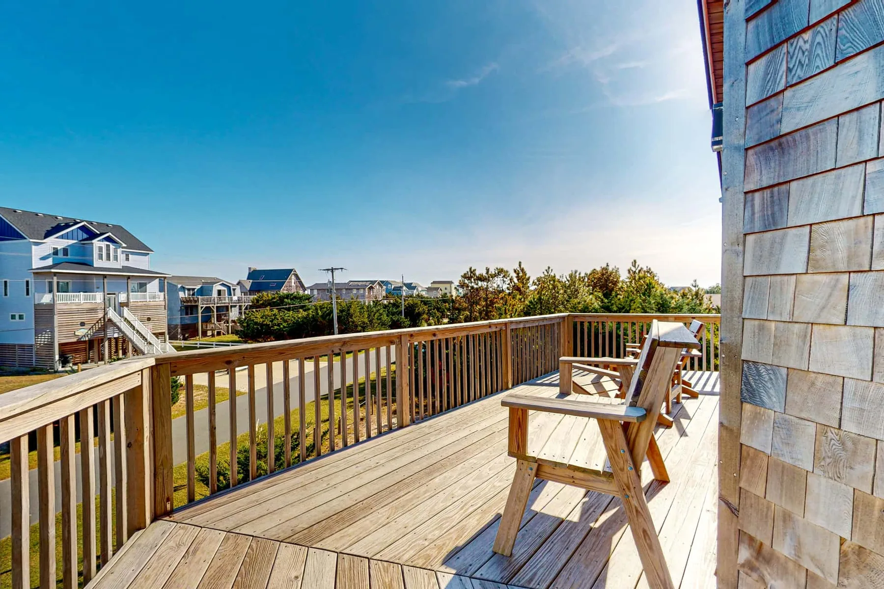 A wooden deck with seating overlooks nearby houses and greenery.