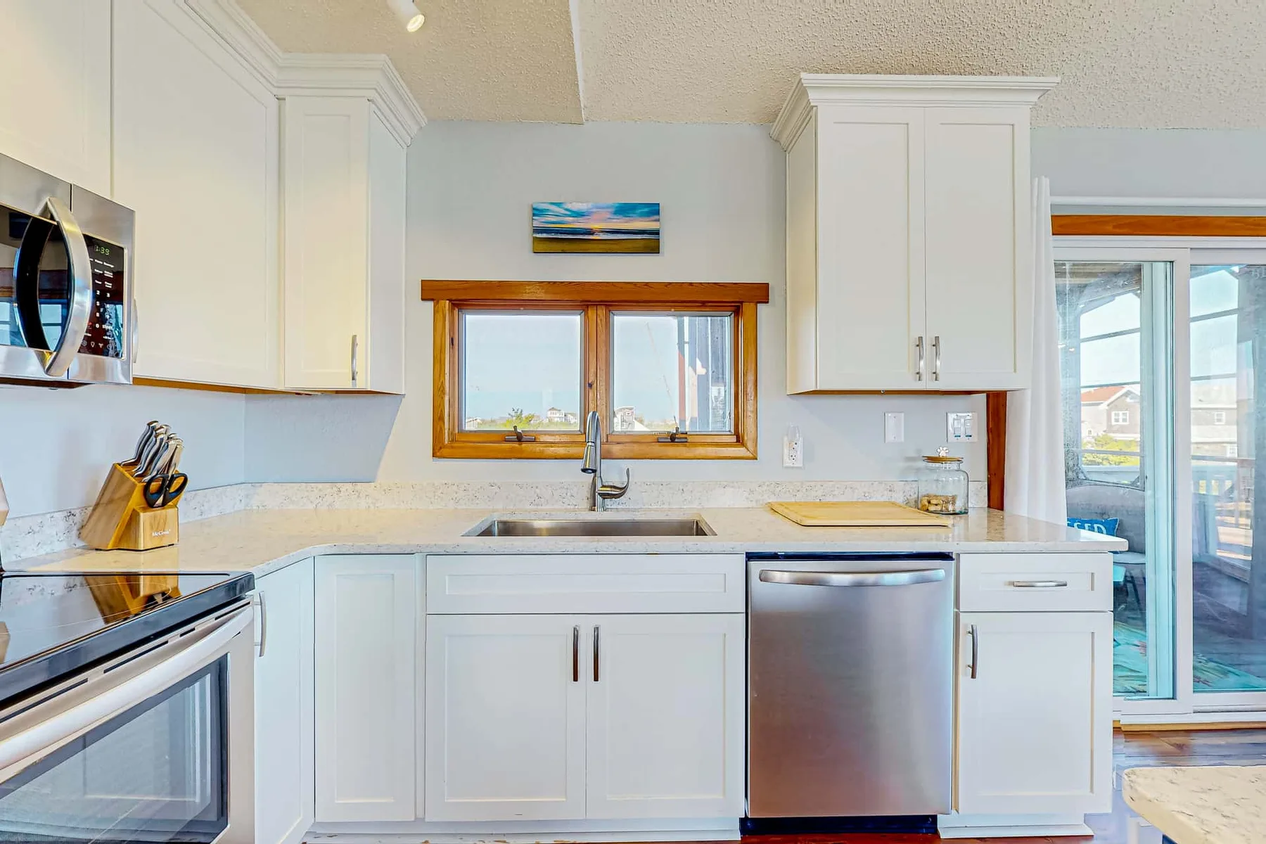 A bright kitchen with white cabinetry, a sink beneath a window, and stainless-steel appliances.