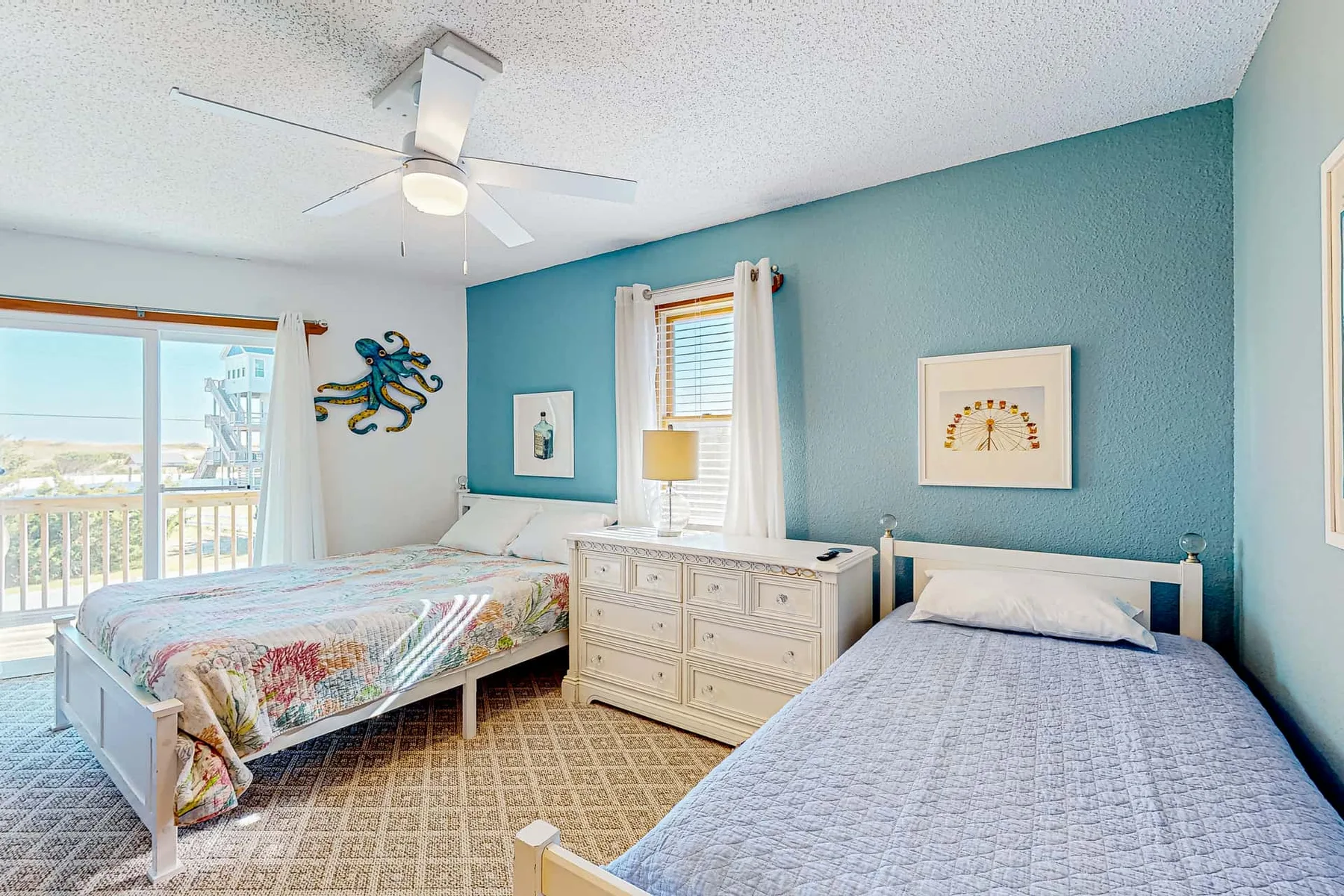 A bedroom with two beds, a dresser, and windows overlooking the water.