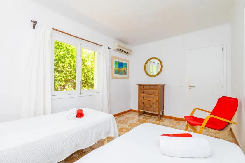 Bright bedroom with two beds, a window, and a wooden dresser.