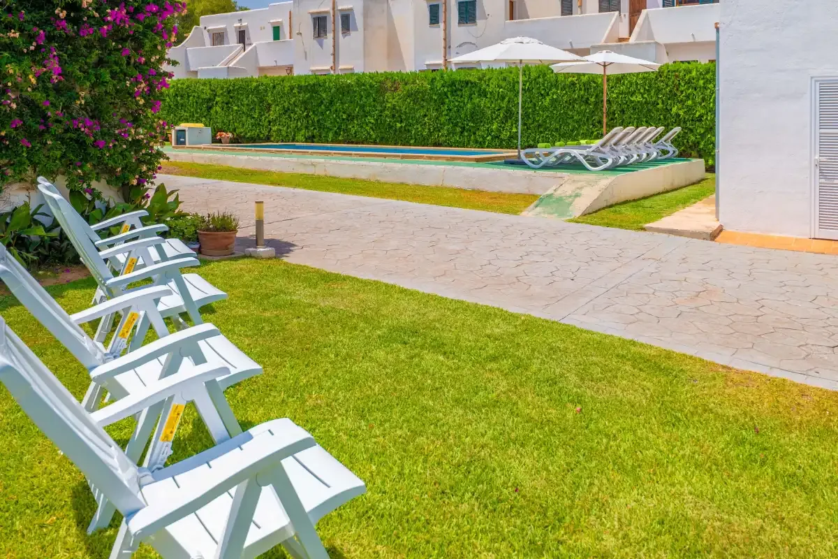 Outdoor pool area with lounge chairs beside a paved walkway and lawn.