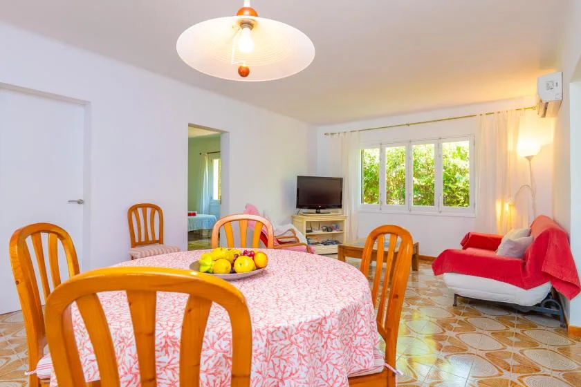 A dining area with a table, wooden seating, and a television by the window.