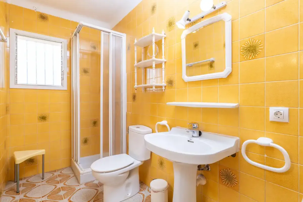 A bathroom with yellow tiled walls, a shower, and a sink.